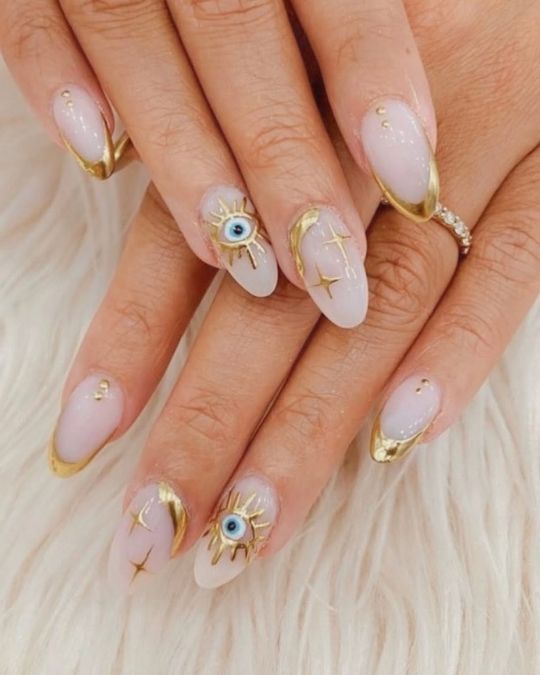 Almond-shaped nails with translucent pink polish, gold tips, evil eye designs.