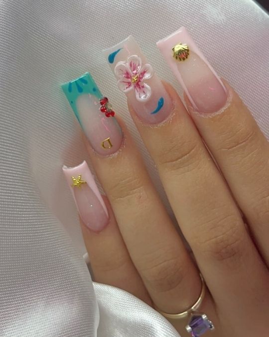 square nails with 3D flower, gold charms, and teal accents.